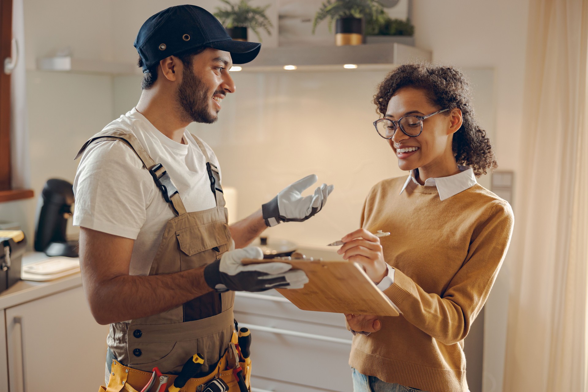 Mulher jovem sorridente assinando documento enquanto se comunica com faz-tudo na cozinha