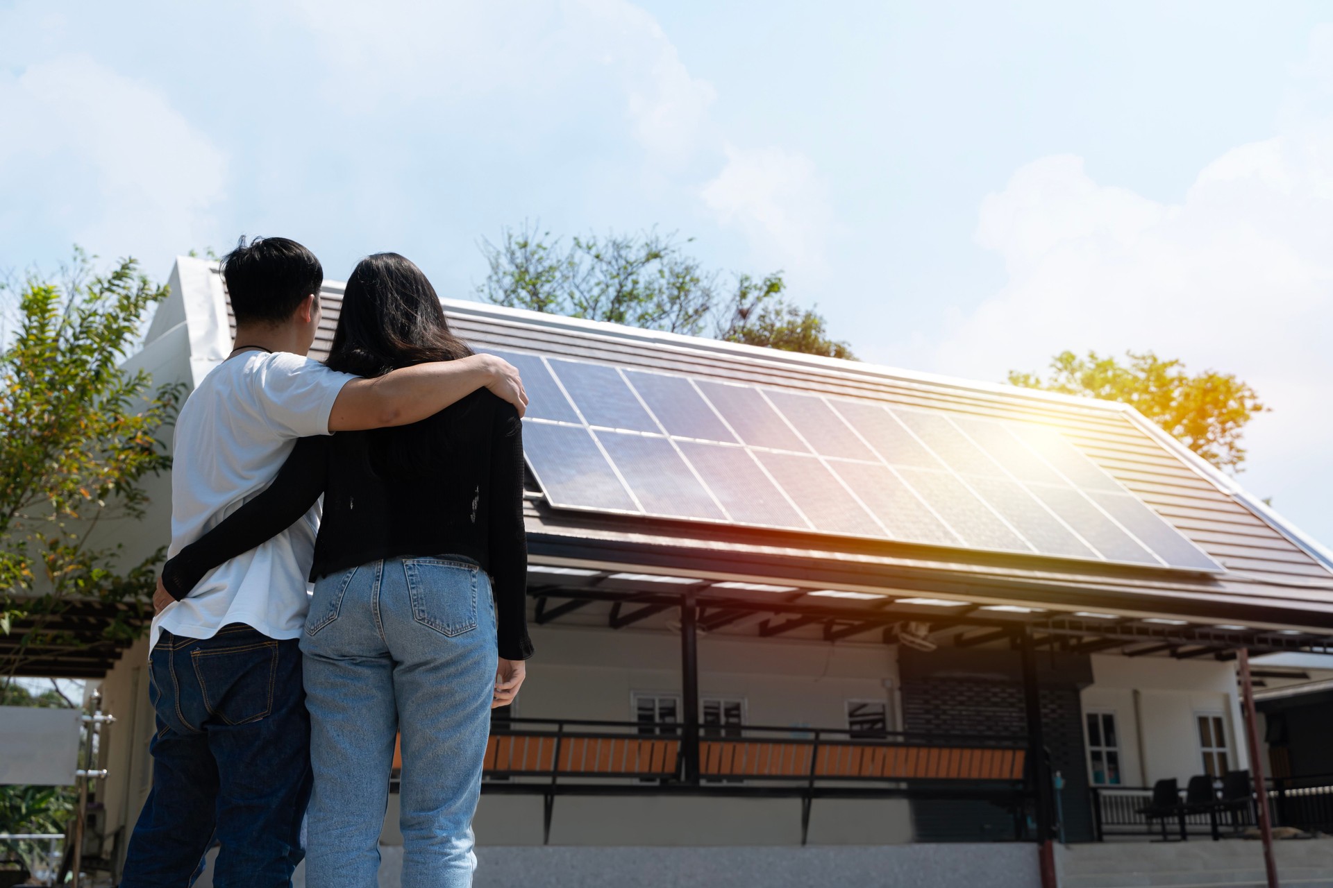 Casal feliz se levantando perto de sua casa com painéis solares. Energia alternativa, economia de recursos e conceito de estilo de vida sustentável.